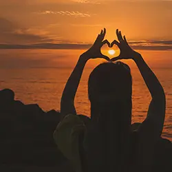 Woman forming heart shape with hands at sunset - cardiovascular health support from curcumin